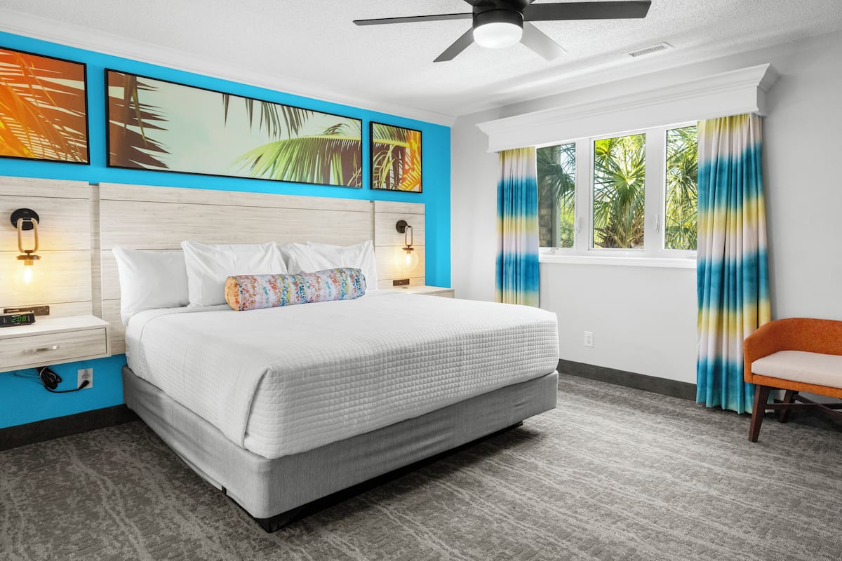 A bedroom with a bed, nightstands, a ceiling fan, a window with curtains, and a chair.