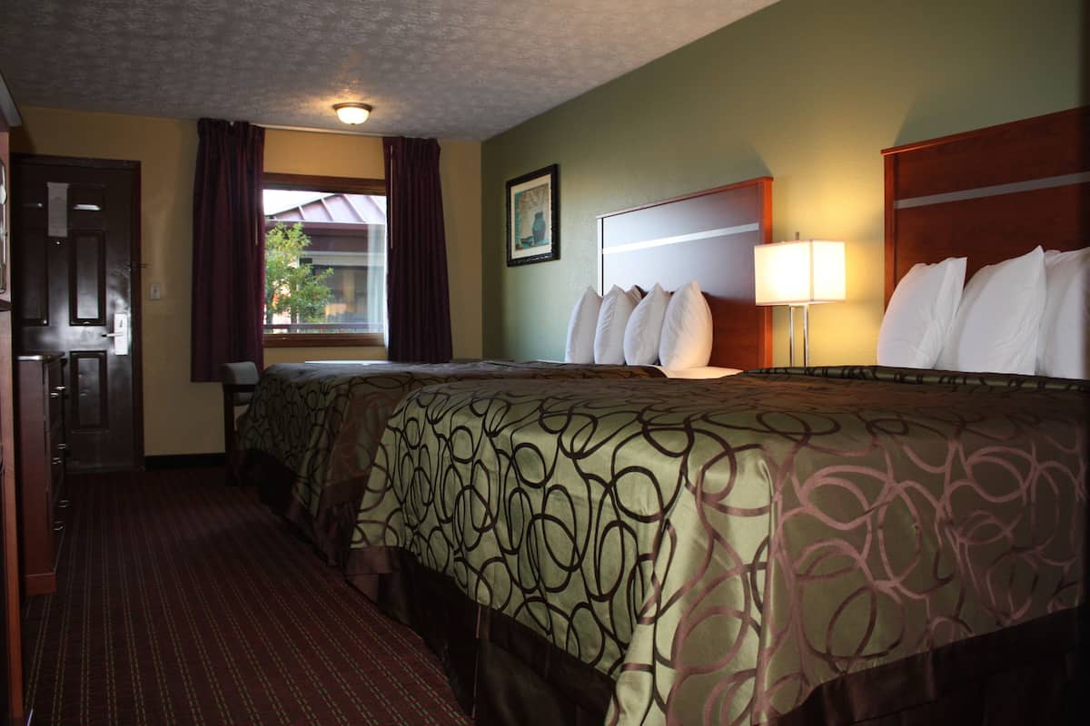 Une chambre d’hôtel avec un grand lit, un bureau, une chaise, une fenêtre avec des rideaux et une lampe.