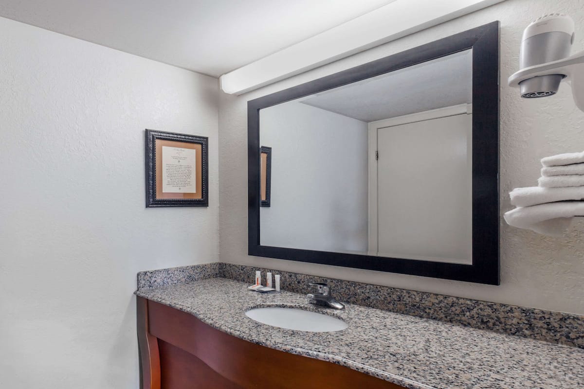 Une salle de bain avec un lavabo doté d’un plan de travail en granit, un grand miroir et un certificat encadré accroché au mur.