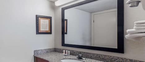 A bathroom with a granite countertop sink, a large mirror, and a framed certificate on the wall.