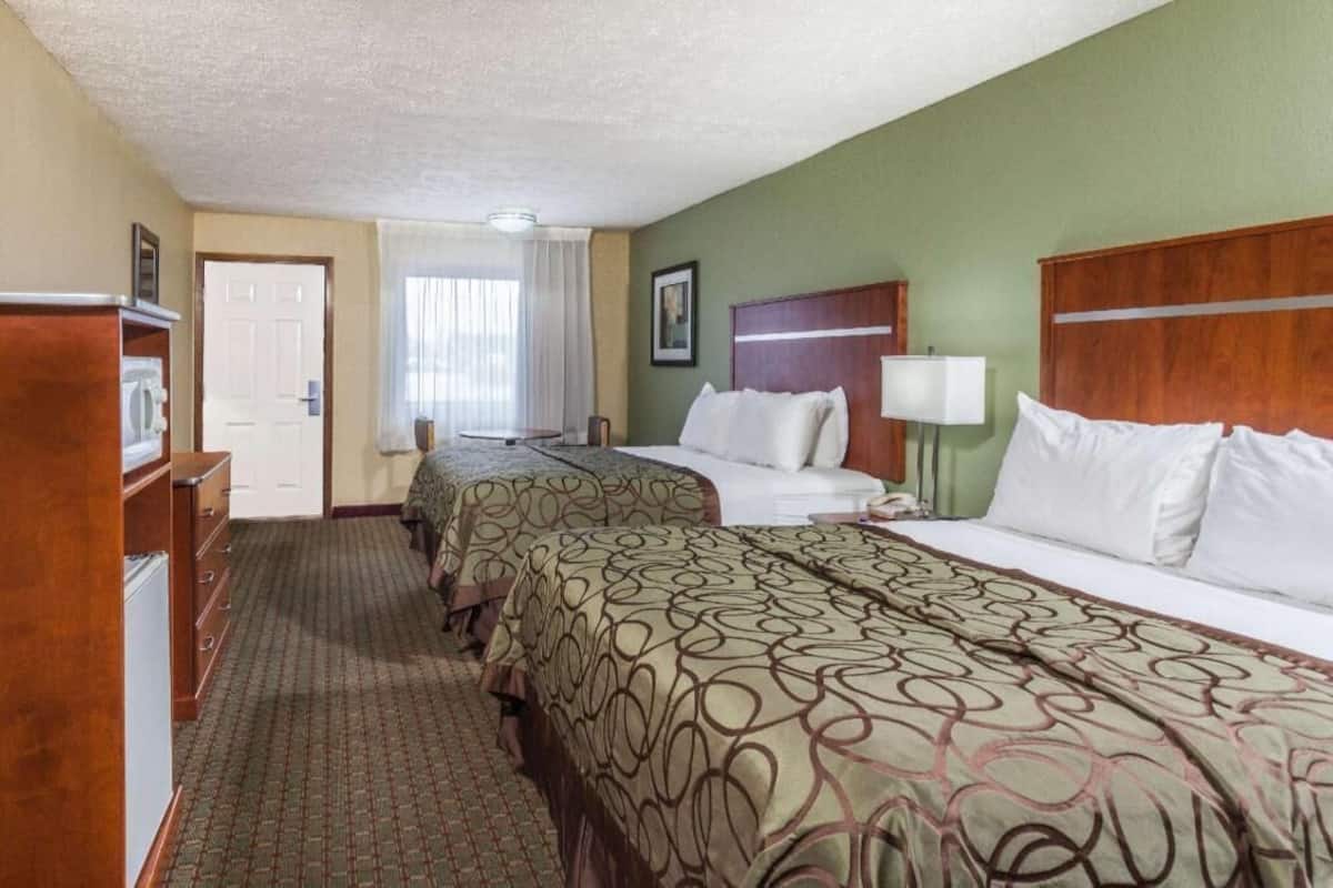 Une chambre d’hôtel avec deux lits, un bureau, une chaise, une lampe et une porte.