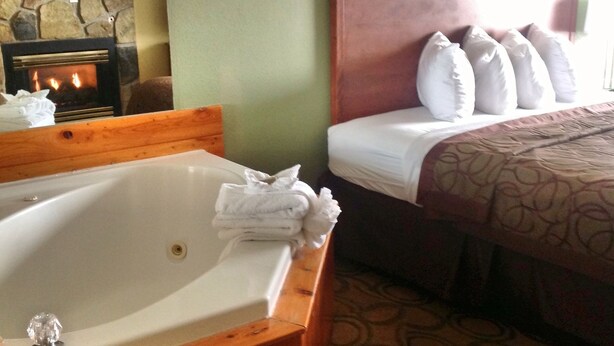 Habitación de hotel con una bañera grande, una cama con almohadillas blancas y una alfombra estampada.