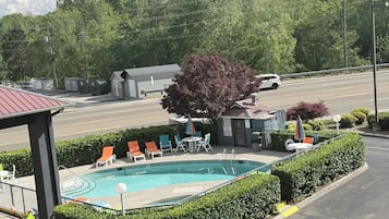 A swimming pool with lounge chairs, a small building, and a road with vehicles.