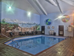 Ein Hallenbad mit Wandgemälde einer Berglandschaft, einer Sitzgelegenheit mit Stühlen sowie einer Wand mit einem Kreisdiagramm und Hinweisschildern für Notausgänge.