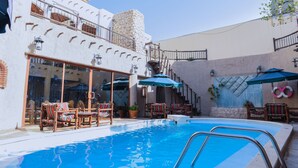A pool area with lounge chairs and umbrellas, a stone tower, and a building with large windows and a balcony. - Al Liwan Suites (Doha)