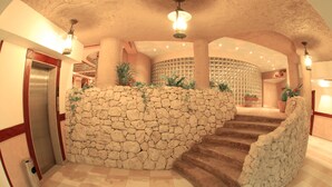 A lobby with a stone wall, a staircase, and an elevator. - Al Liwan Suites (Doha)