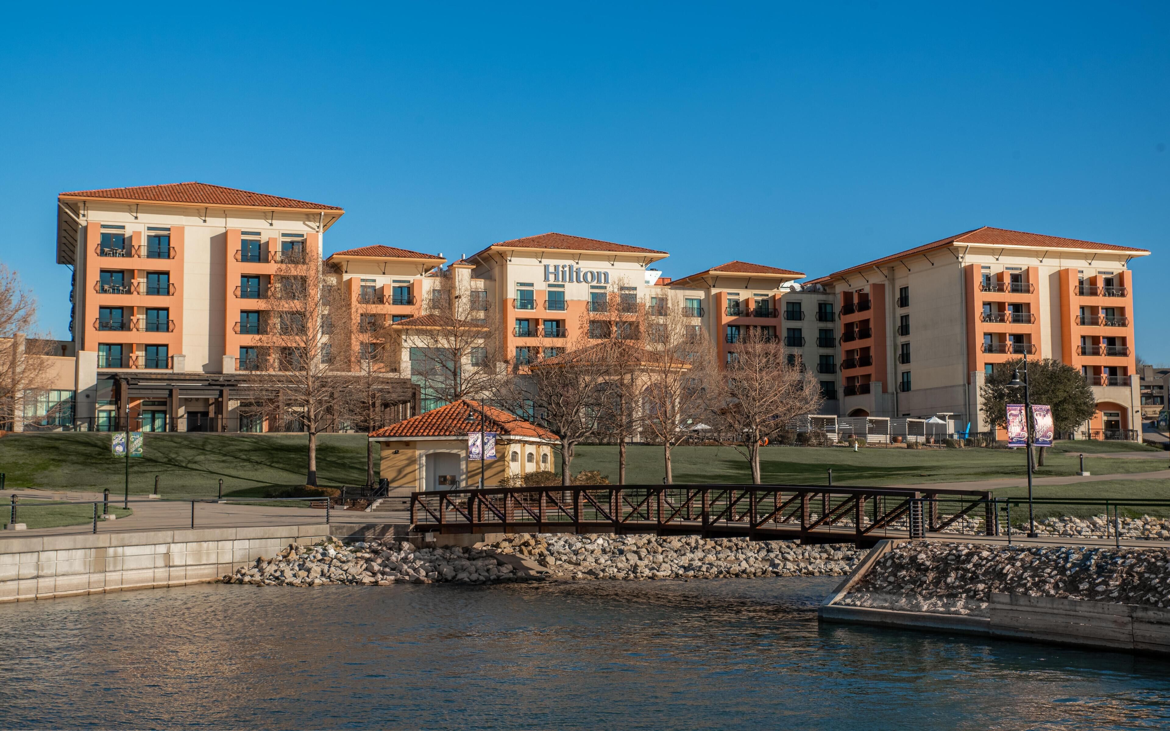 A multi-story hotel with a tiled roof, a swimming pool, and a bridge over water.