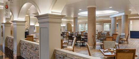A spacious hotel lobby with multiple seating areas, a stone reception desk, and a sign indicating the name of the hotel.