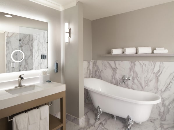 Une salle de bain moderne avec un lavabo en marbre, une baignoire sur pieds et un miroir doté d’un cadre circulaire.