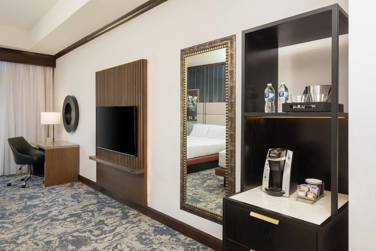 A hotel room with a TV, a large mirror, a coffee maker, and a minibar.