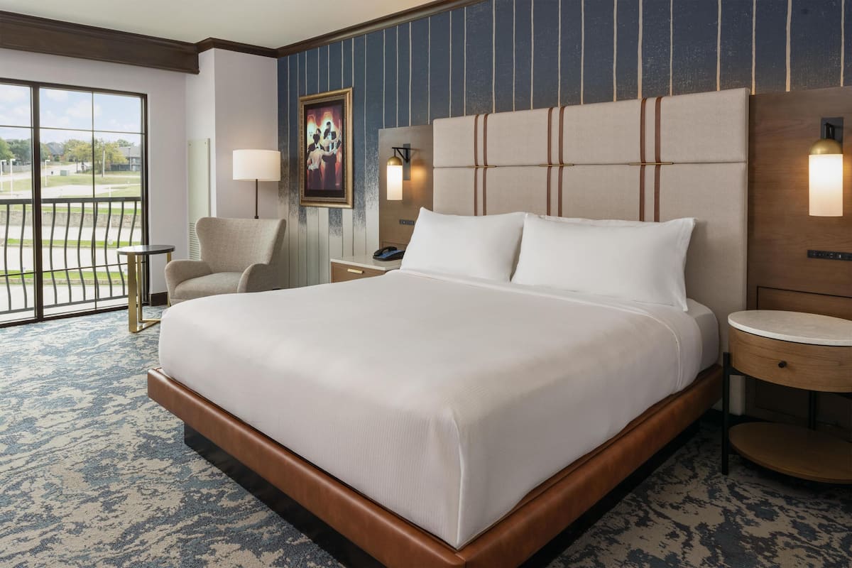 A hotel room with a large bed, a chair, a small table, a lamp, and a painting on the wall.