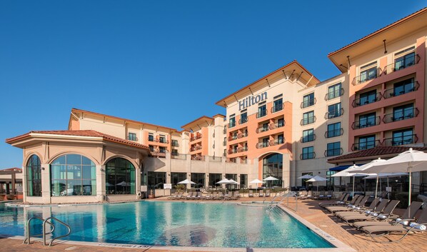A hotel with a swimming pool, multiple balconies, and outdoor seating areas. - Hilton Dallas/Rockwall Lakefront (Rockwall)