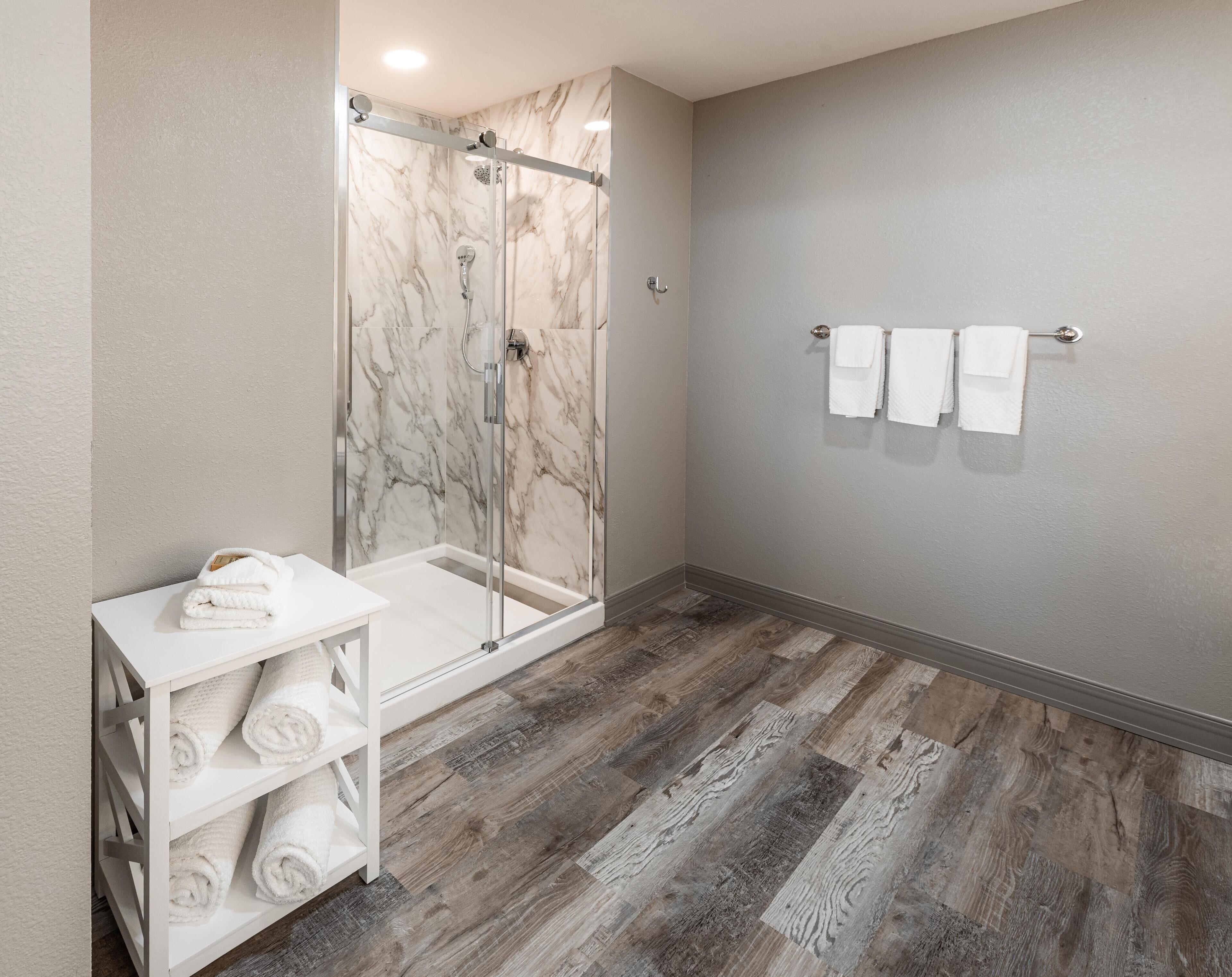A bathroom with a glass-enclosed shower, a white shelf with towels, and a wall-mounted towel rack.