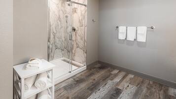 A bathroom with a glass-enclosed shower, a white shelf with towels, and a wall-mounted towel rack.
