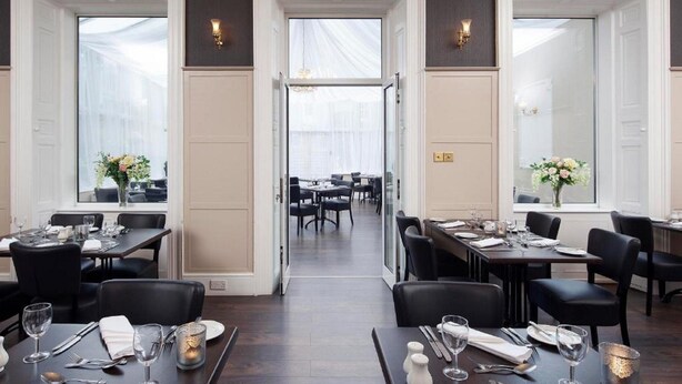 A formal dining area with tables set for service, large windows, and a view into the dining room. - Elfordleigh (Plymouth)