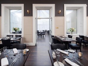 A formal dining area with tables set for service, large windows, and a view into the dining room. - Elfordleigh (Plymouth)