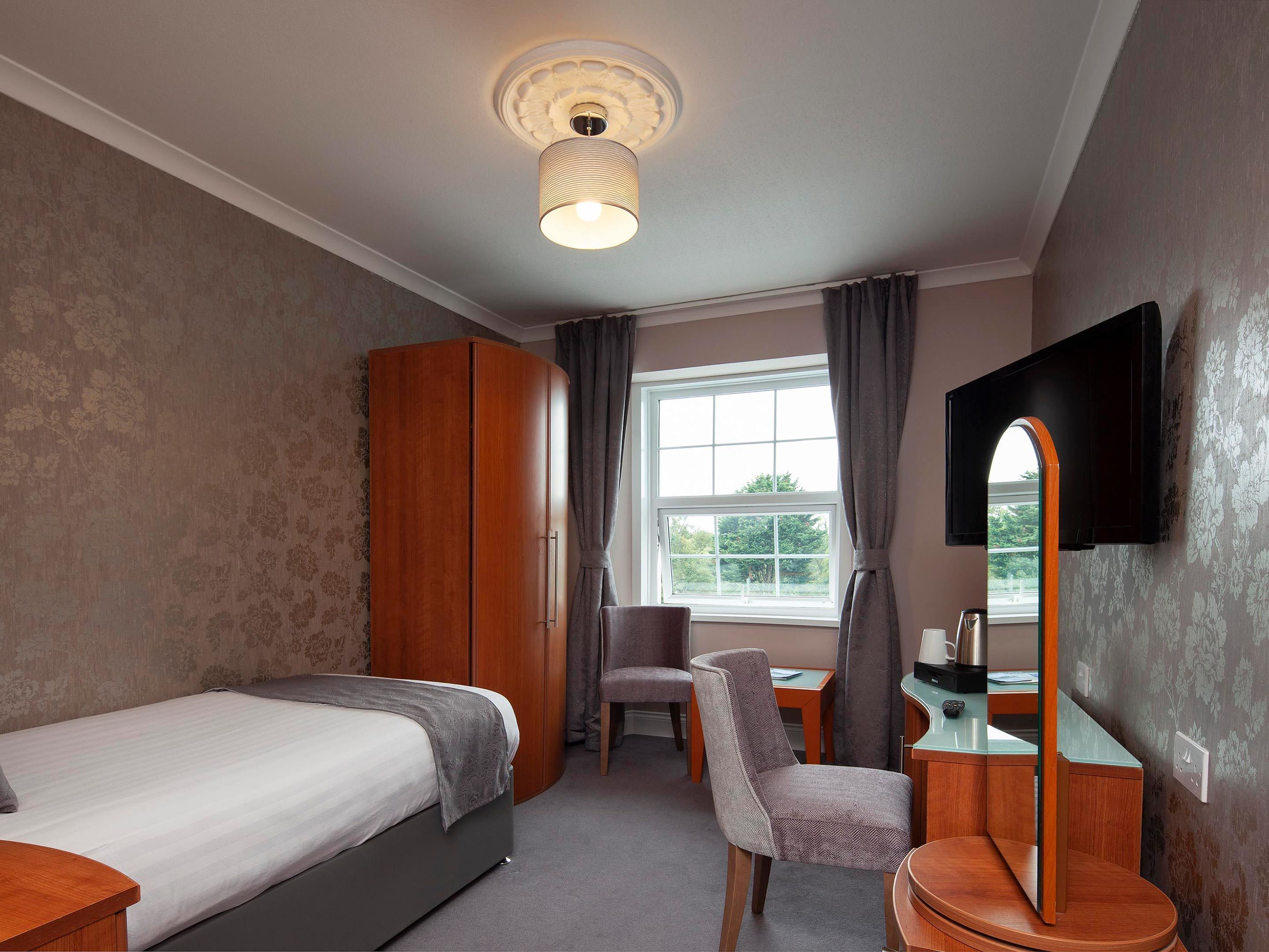 Une chambre d’hôtel équipée d’un lit, d’un bureau, d’une chaise, d’une armoire, d’une télévision et d’une fenêtre avec des rideaux.
