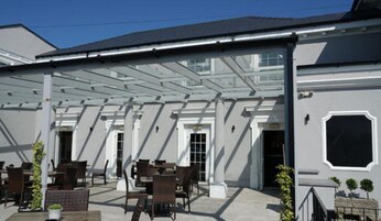 An outdoor patio area with tables and chairs, covered by a white pergola.