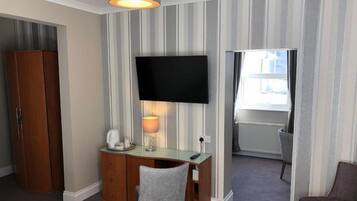Habitación de hotel con escritorio, silla, televisor, armario y vistas al exterior.