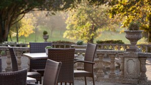 An outdoor seating area with wicker chairs and tables, surrounded by stone balustrades and greenery. - Elfordleigh (Plymouth)
