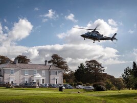 A helicopter flying over a building with a parking lot and a golf course in the foreground.
