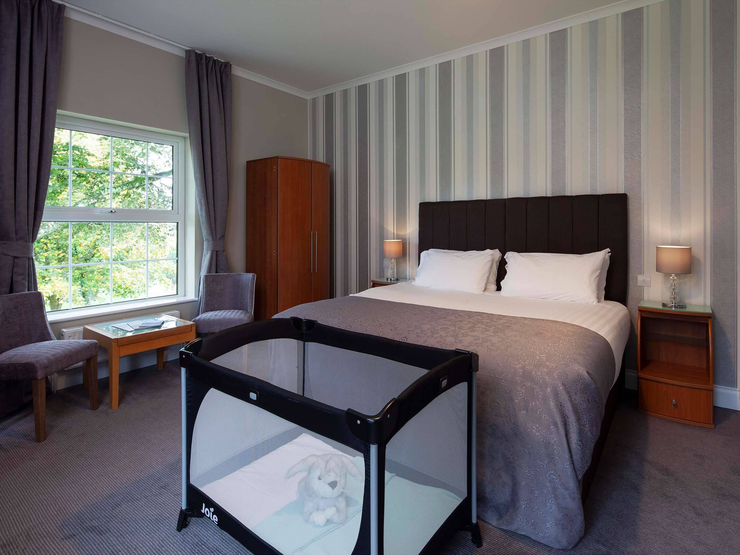 A hotel room with a large bed, a desk, a chair, a wardrobe, and a window with curtains.