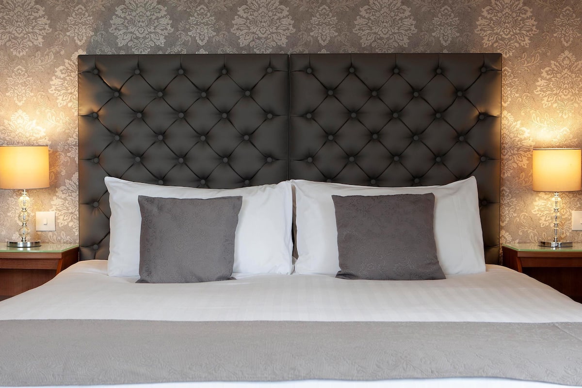 A bed with a tufted headboard, two bedside tables with lamps, and a patterned wallpaper.