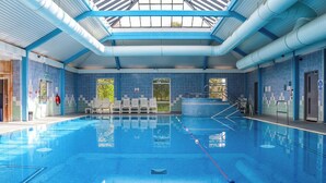 A large indoor swimming pool with clear blue water, a tiled floor, and a roof structure. - Elfordleigh (Plymouth)
