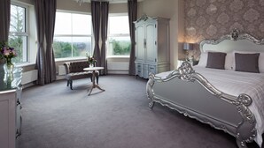 A bedroom with a large bed, a dresser, a vanity, and a window with curtains. - Elfordleigh (Plymouth)