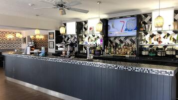 A bar area with a counter, bar stools, a ceiling fan, and a television screen displaying a sports game.