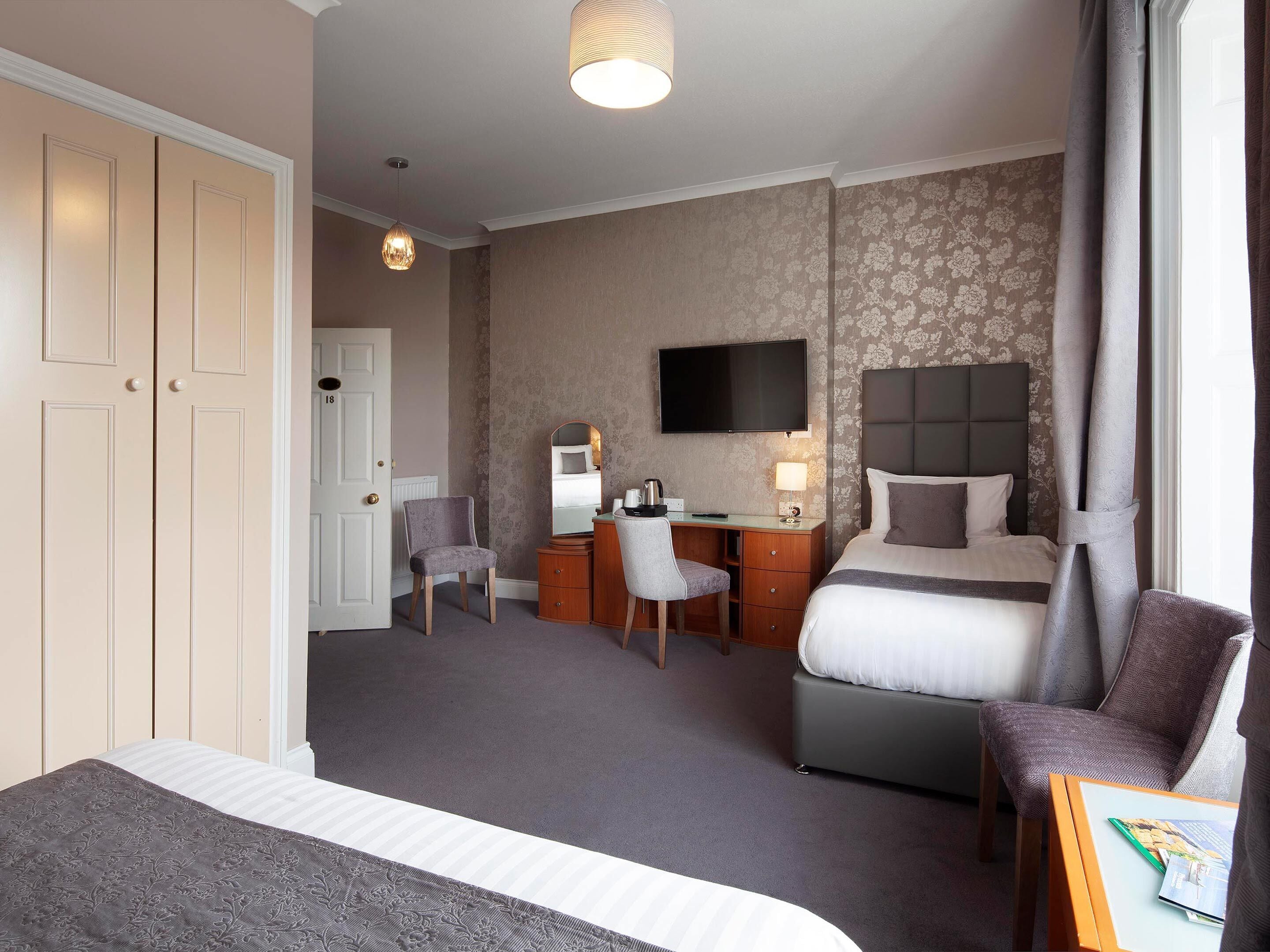 A hotel room with a bed, a desk, a chair, a television, and a door.