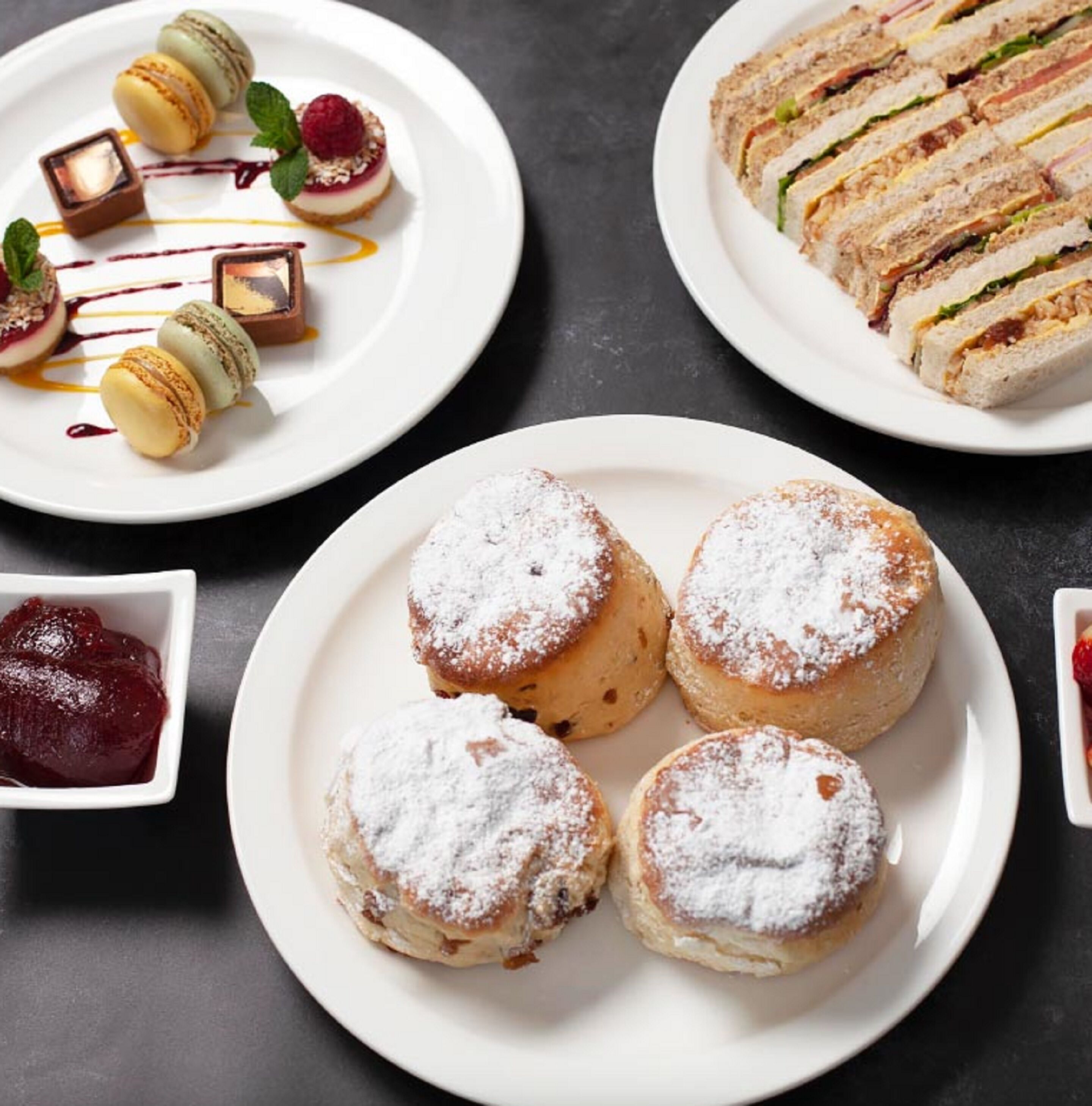 A variety of desserts including macarons, a layered sandwich, and scones dusted with powdered sugar.