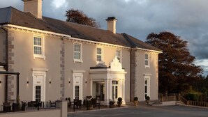 A large, two-story building with a symmetrical facade, featuring a central entrance with a decorative pediment, multiple windows, and a parking area in front. - Elfordleigh (Plymouth)