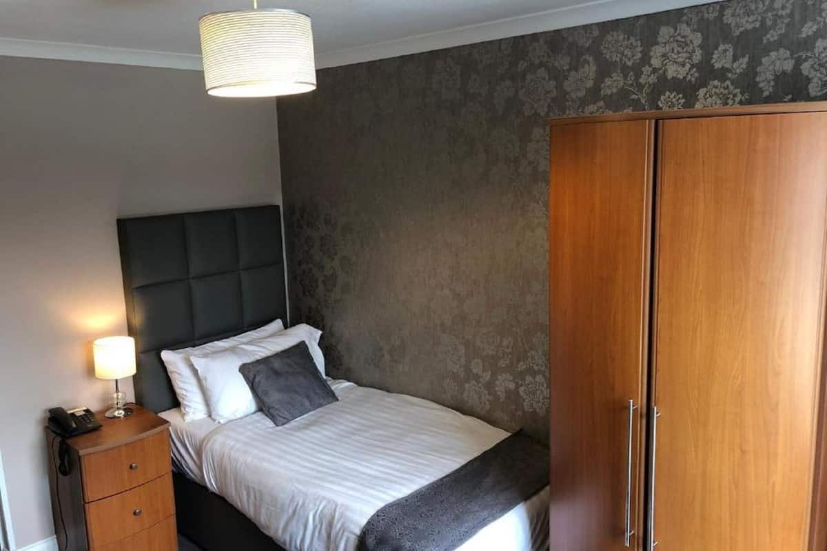A bedroom with a bed, bedside table, lamp, and wardrobe.