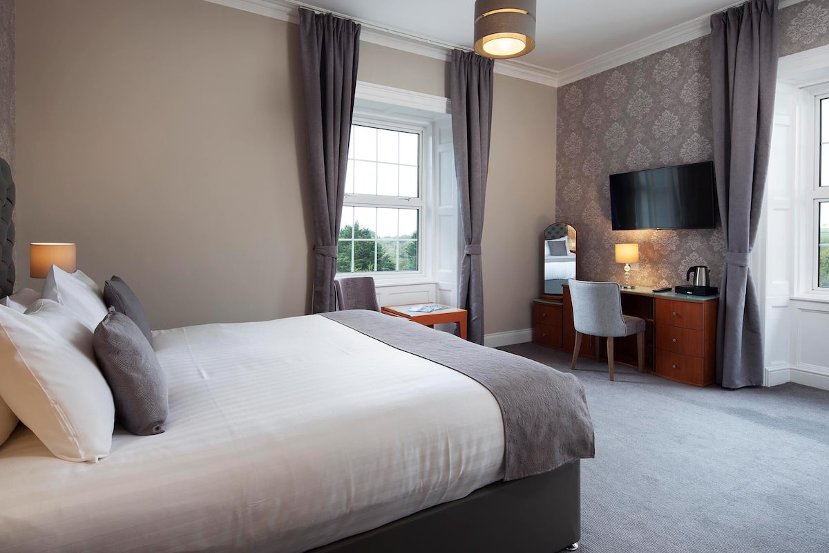 A hotel room with a large bed, a desk, a chair, a television, and a window with curtains.