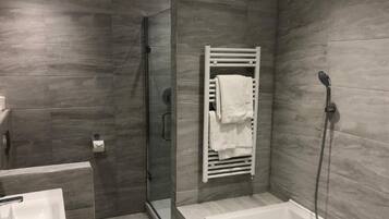 A modern bathroom with a glass shower enclosure, a built-in towel rack, a bathtub, and a sink.