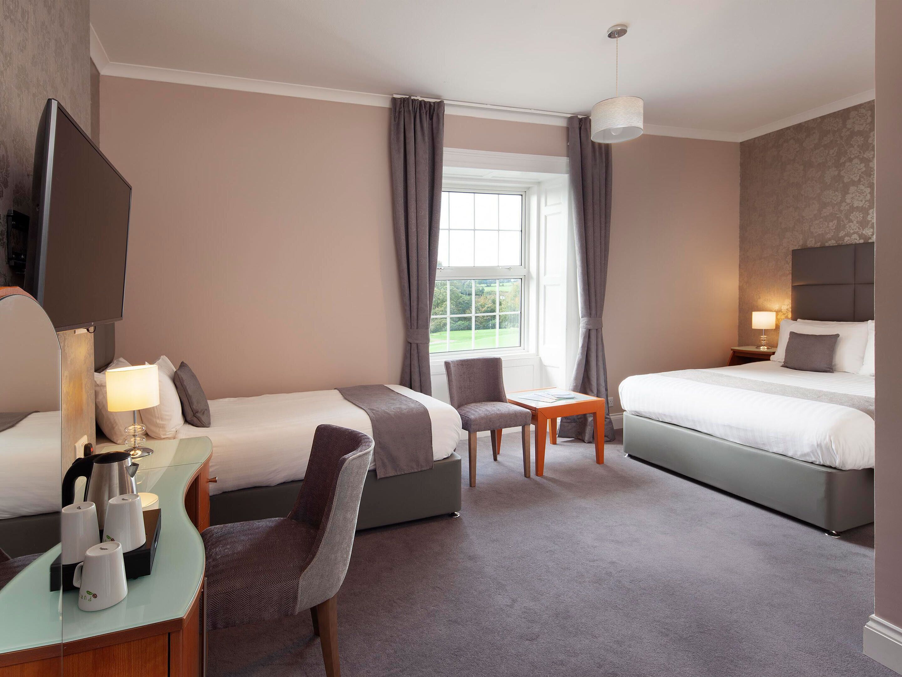 A hotel room with two beds, a desk with a chair, a small table, and a television.