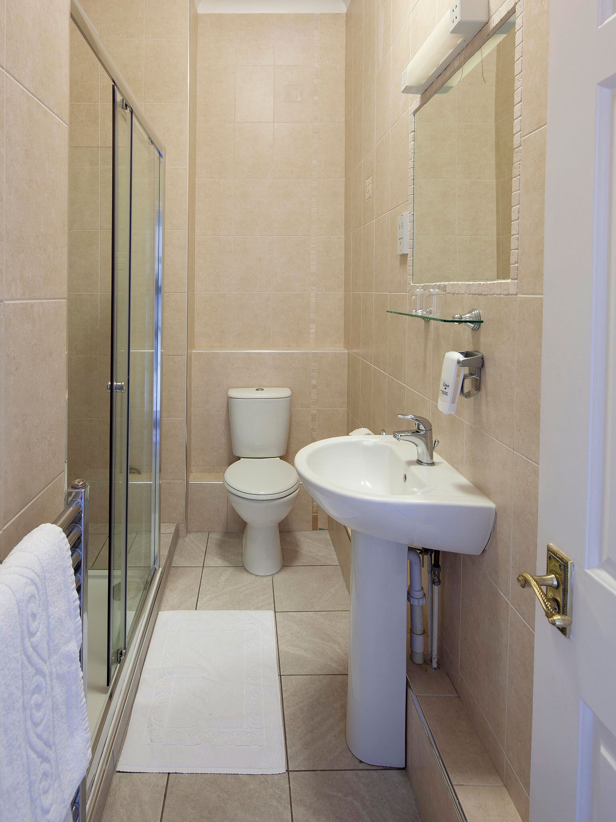 Un baño moderno con cabina de ducha de vidrio, inodoro blanco y lavamanos pedestal.