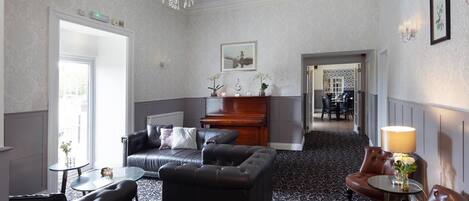 A hotel lobby with a grand piano, leather sofas, a chandelier, and a patterned carpet.
