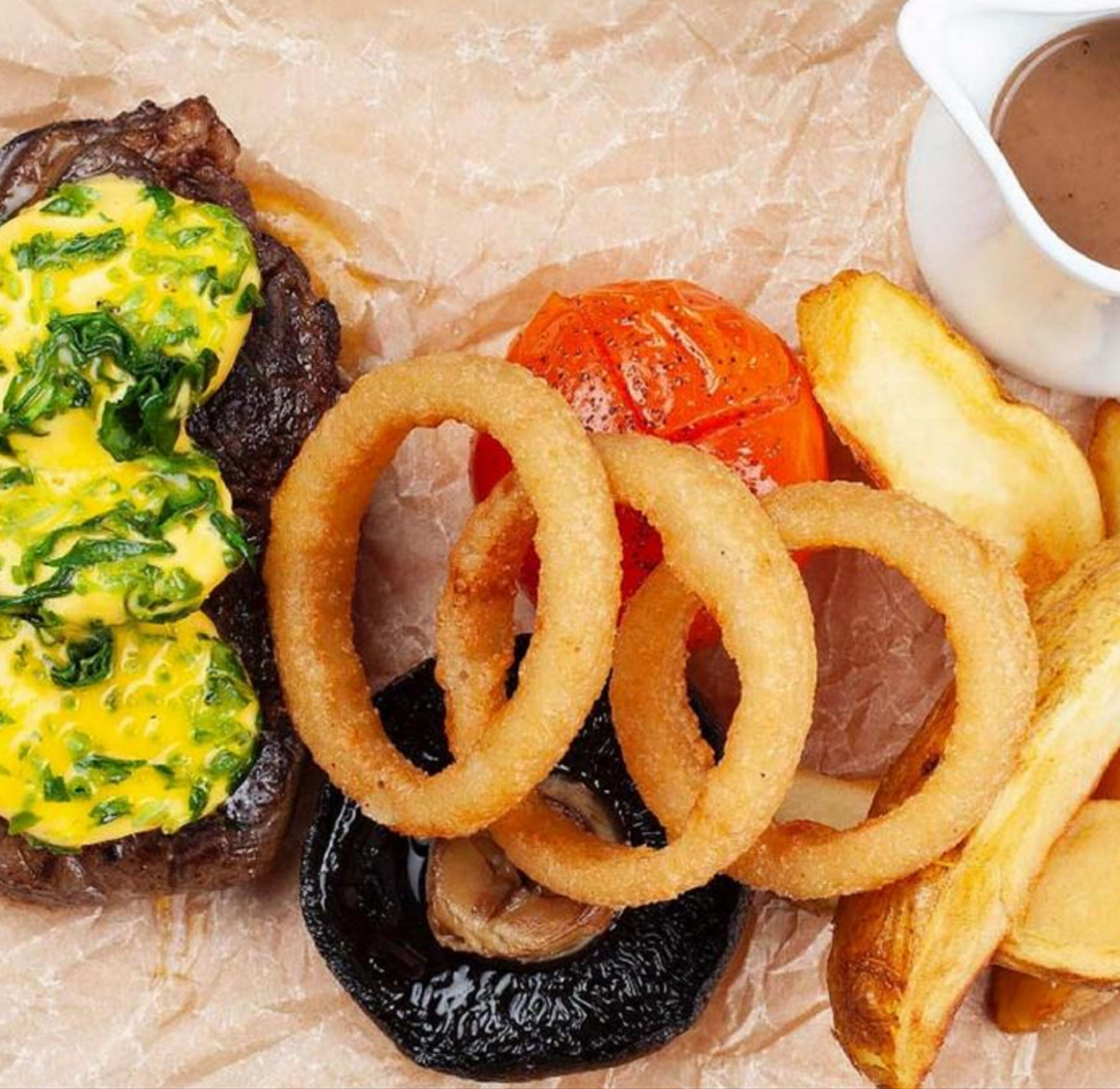 A meal consisting of steak, onion rings, roasted potatoes, and a baked tomato.