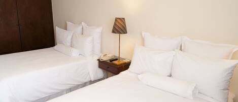 A hotel room with two single beds, a wooden wardrobe, a bedside table with a lamp, and a telephone.