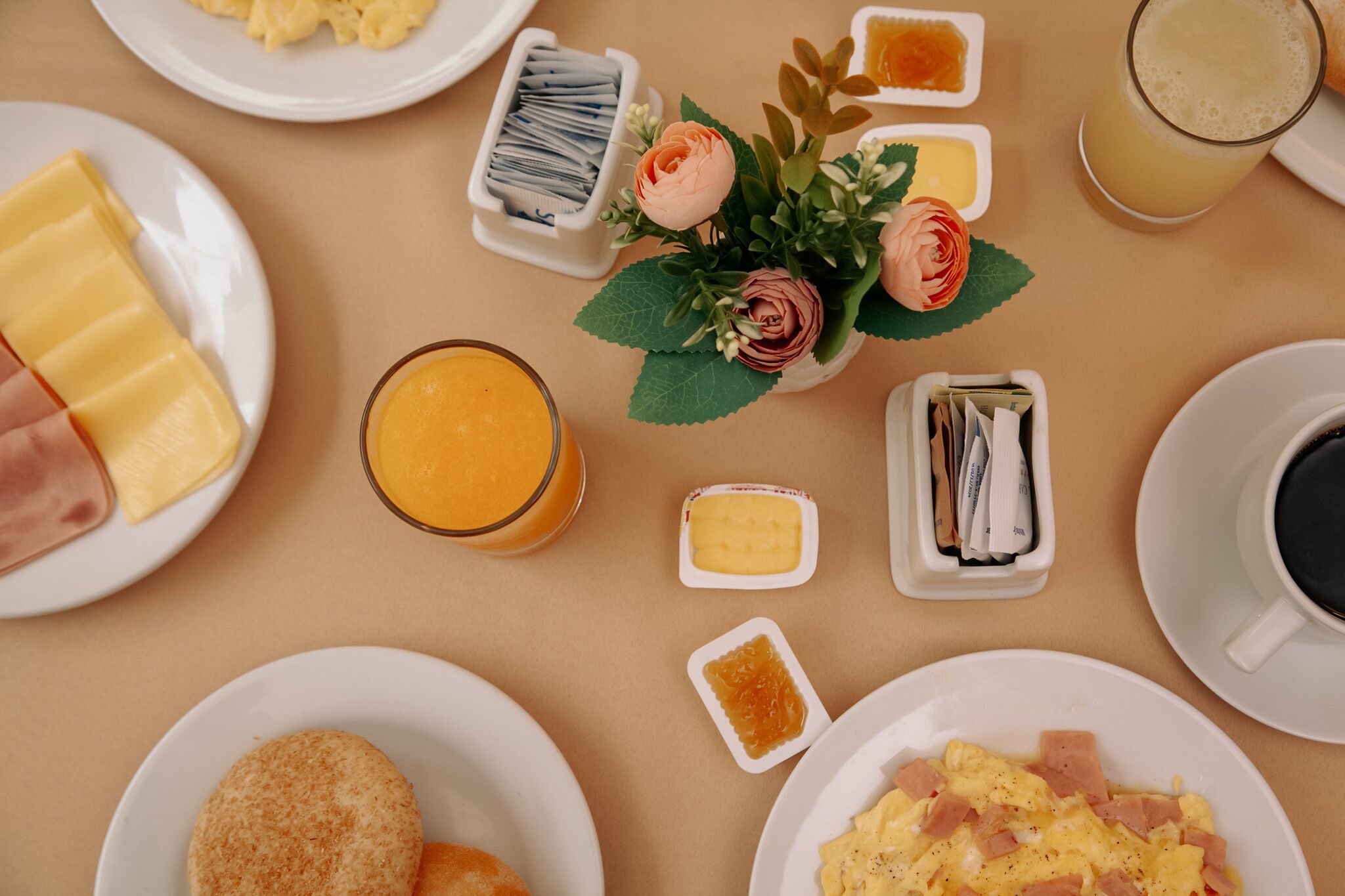 A breakfast setting with plates of food, a glass of orange juice, a cup of coffee, and a small flower arrangement.