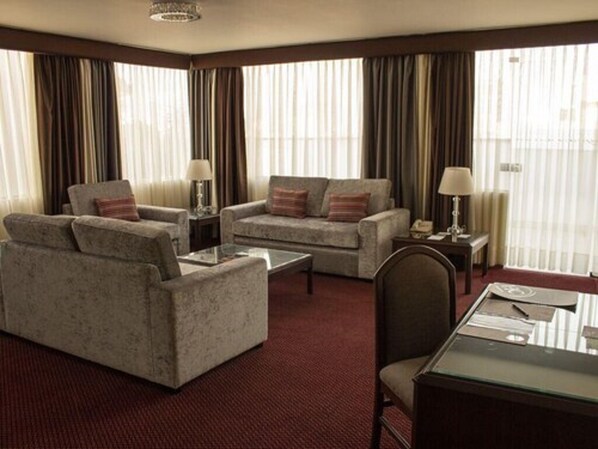 A hotel room with a sofa set, a coffee table, a desk with a chair, and a large window with curtains. - Hotel Carrera SAC (Lima)