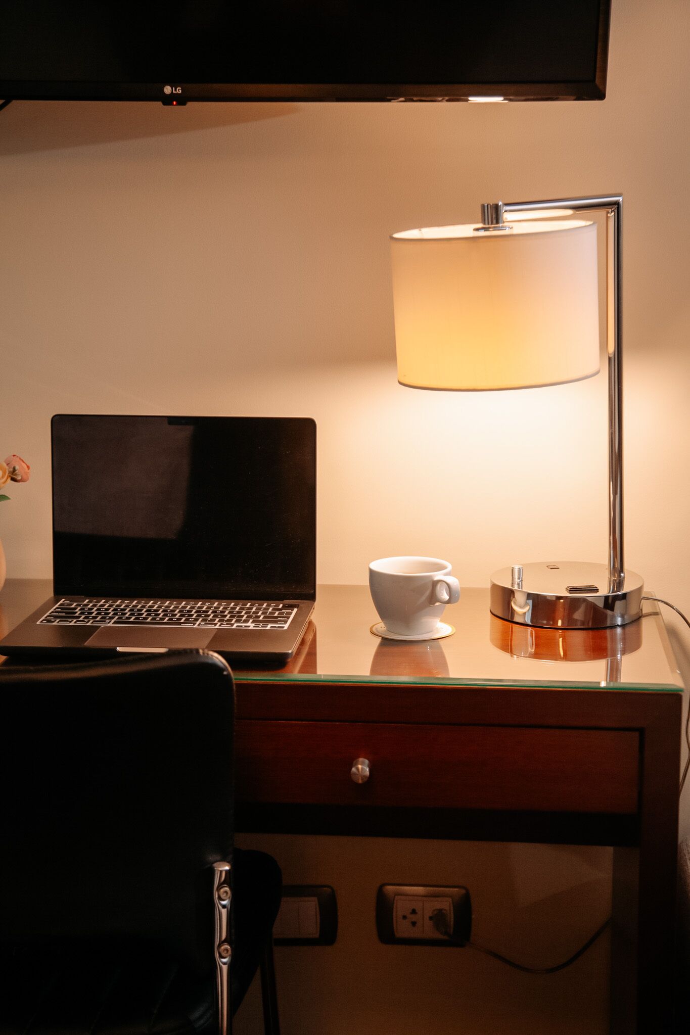 A laptop on a desk with a lamp, a cup, and a drawer.