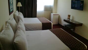 Habitación de hotel con dos camas, un escritorio, televisor y ventana con cortinas.