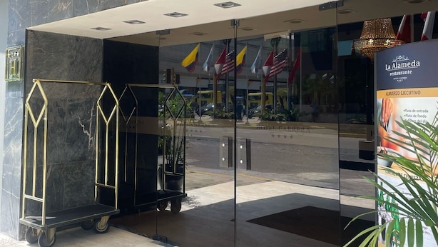 L’entrée de l’hôtel Carrera se distingue par sa façade en marbre, ses portes en verre et un espace de stationnement bien visible.