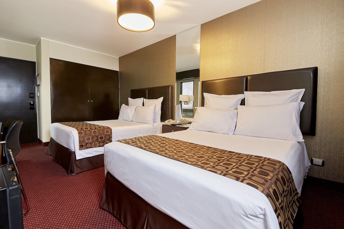 Quarto de hotel com duas camas, uma escrivaninha, uma cadeira e um espelho.