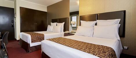 A hotel room with two beds, a desk, a chair, and a mirror.
