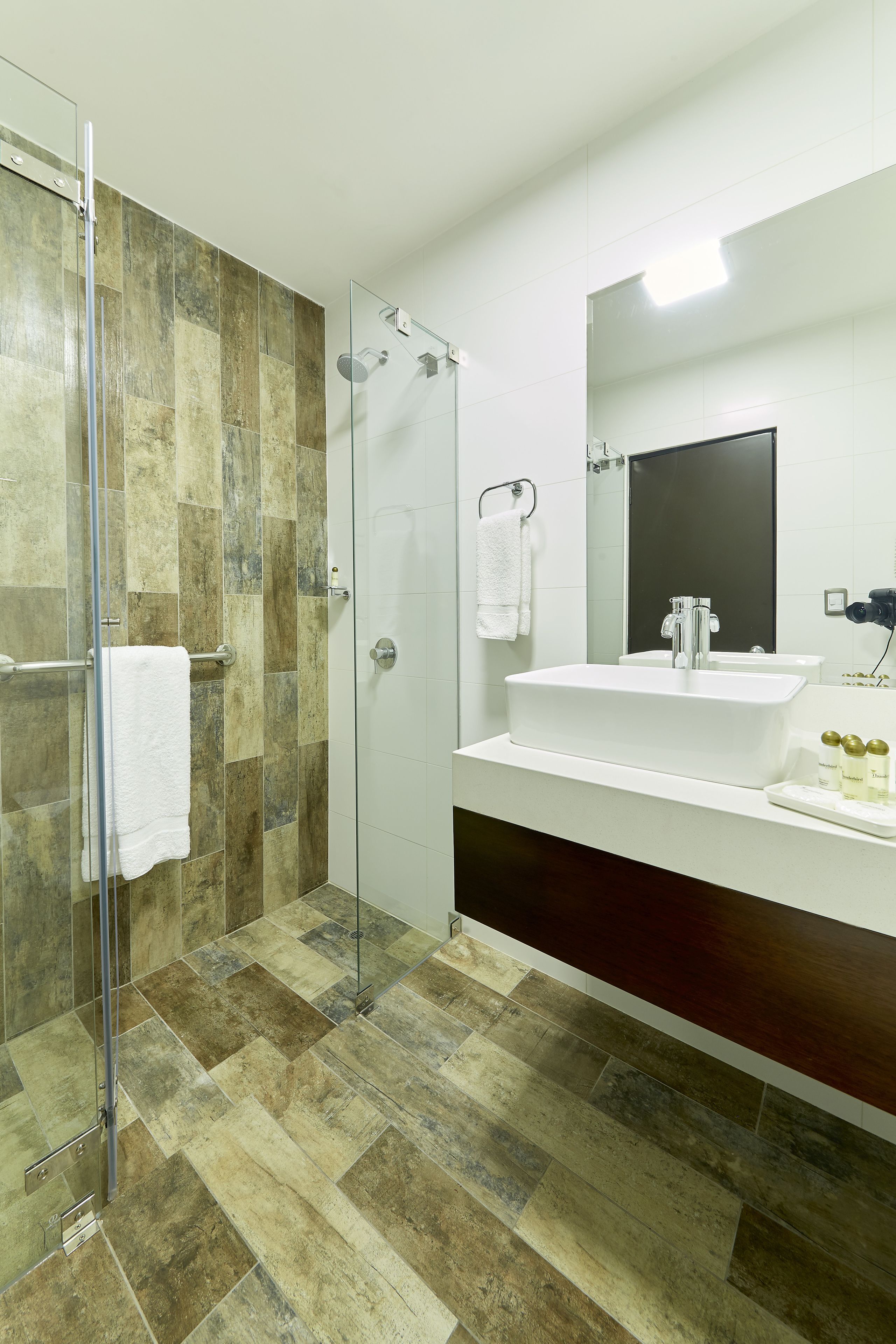 Un baño moderno con cabina de ducha de vidrio, lavabo blanco y un espejo grande.