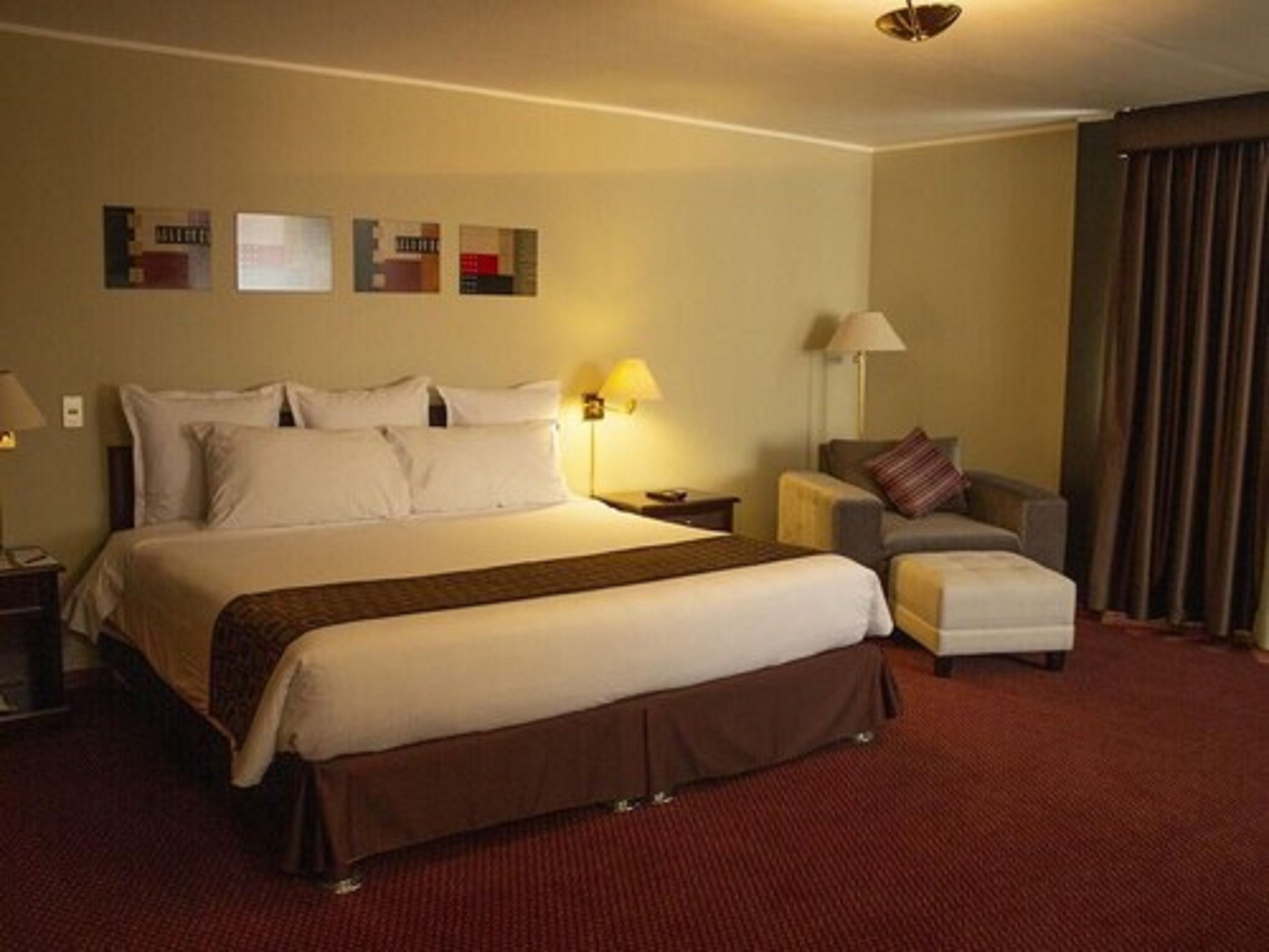 A hotel room with a large bed, a nightstand, a chair, a lamp, and a wall with three framed pictures.